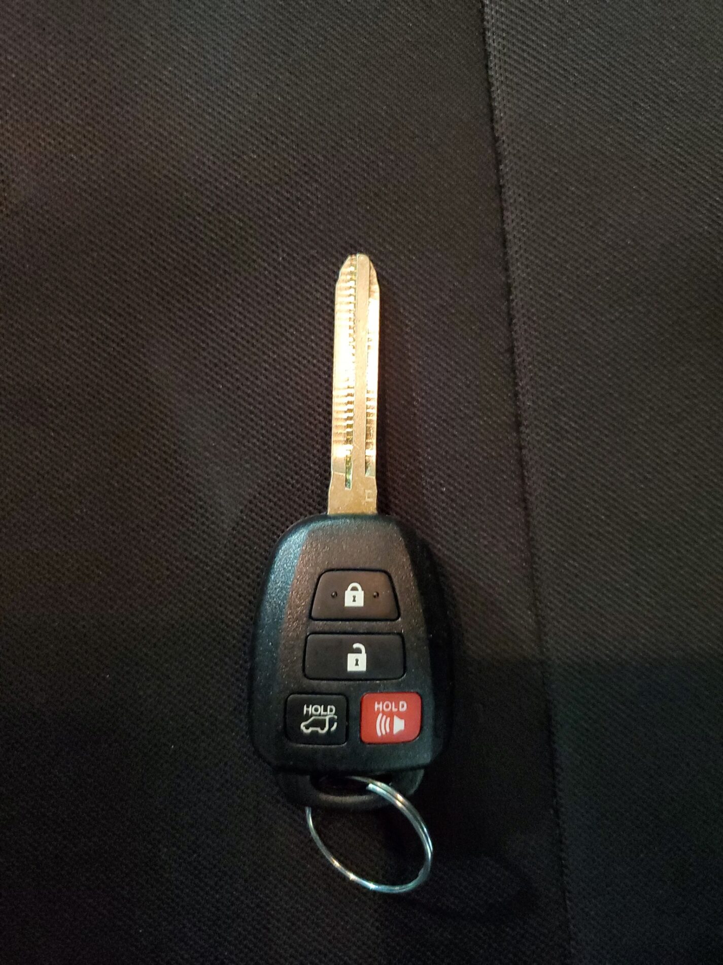 A car key with a black plastic fob featuring four buttons: lock, unlock, trunk, and panic, against a dark background.