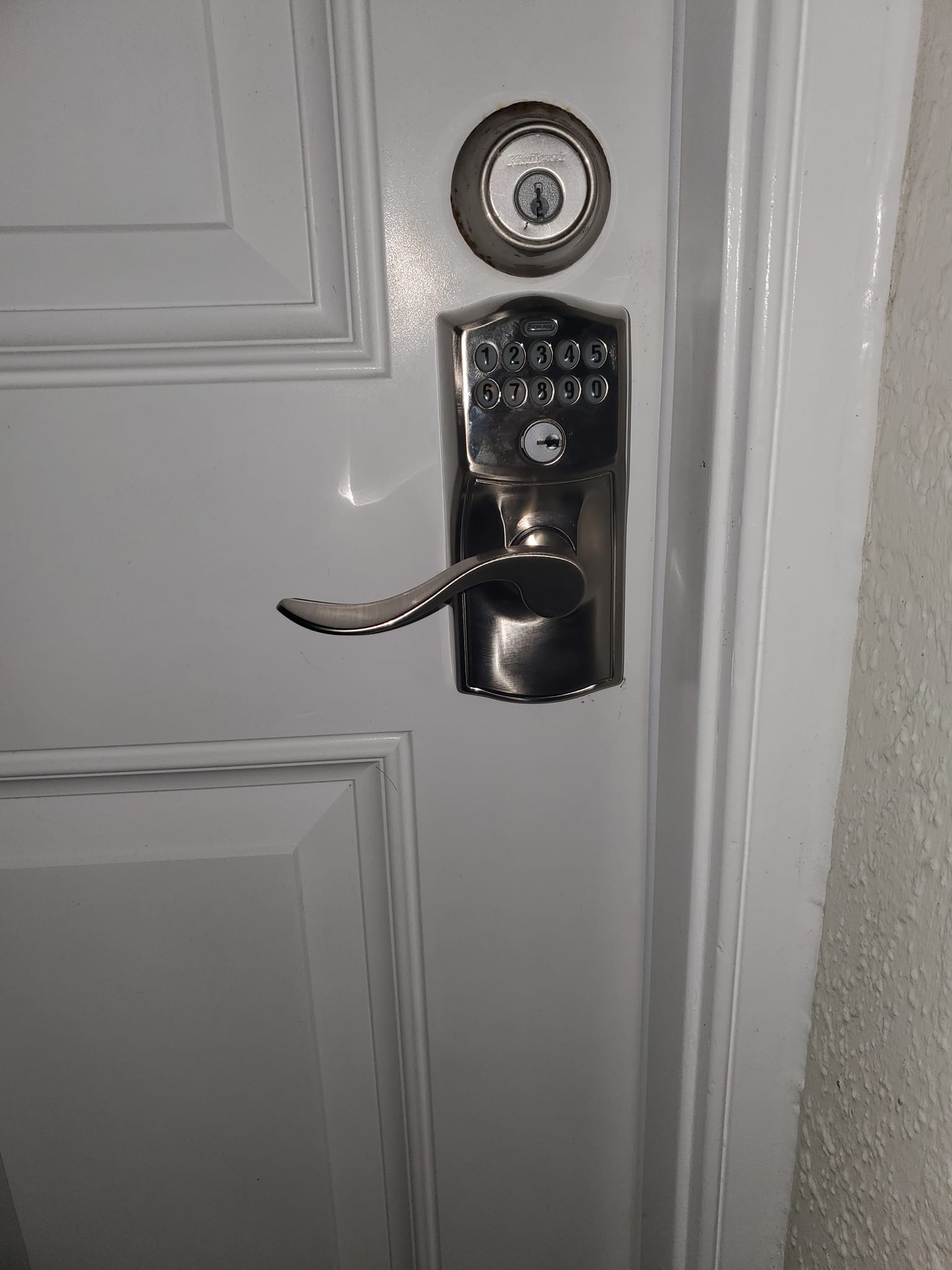 A white door with a silver keypad electronic lock and a lever handle, and a deadbolt above.